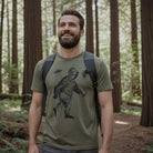 Man wearing a olive green t-shirt with alien bigfoot in a forest