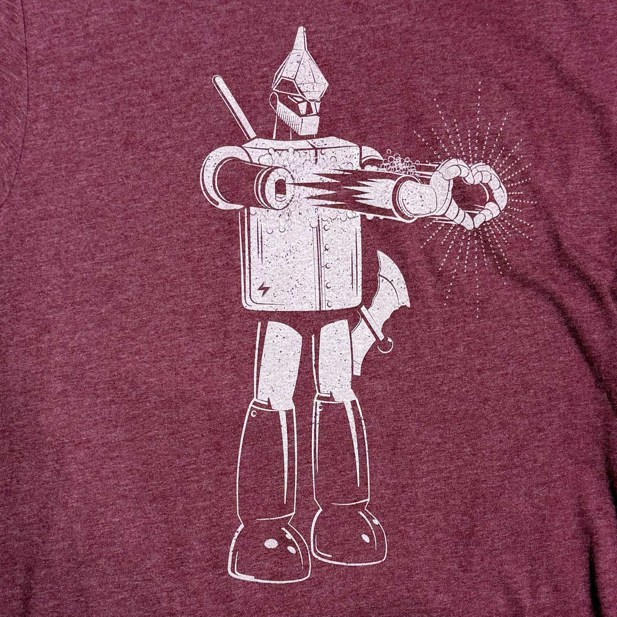 A close-up of a heathered maroon t-shirt featuring a distressed white graphic of the Tin Man from The Wizard of Oz making a heart gesture with his hands.