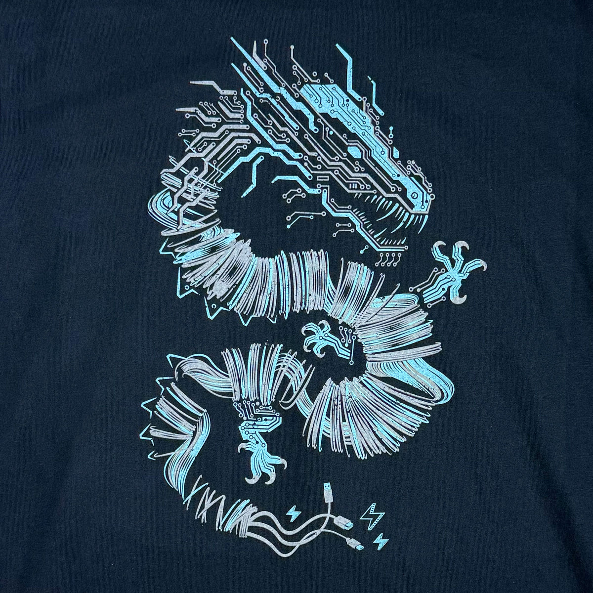 A close-up of a dark navy blue t-shirt featuring a STORY SPARK graphic of a cyber dragon composed of glowing circuitry and lines in light blue, white, and cyan.